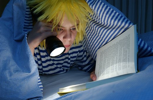 Ein Kind liest ein Buch mit Taschenlampe im Bett